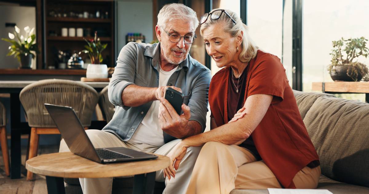 Een ouder stel kijkt op een telefoon en laptop